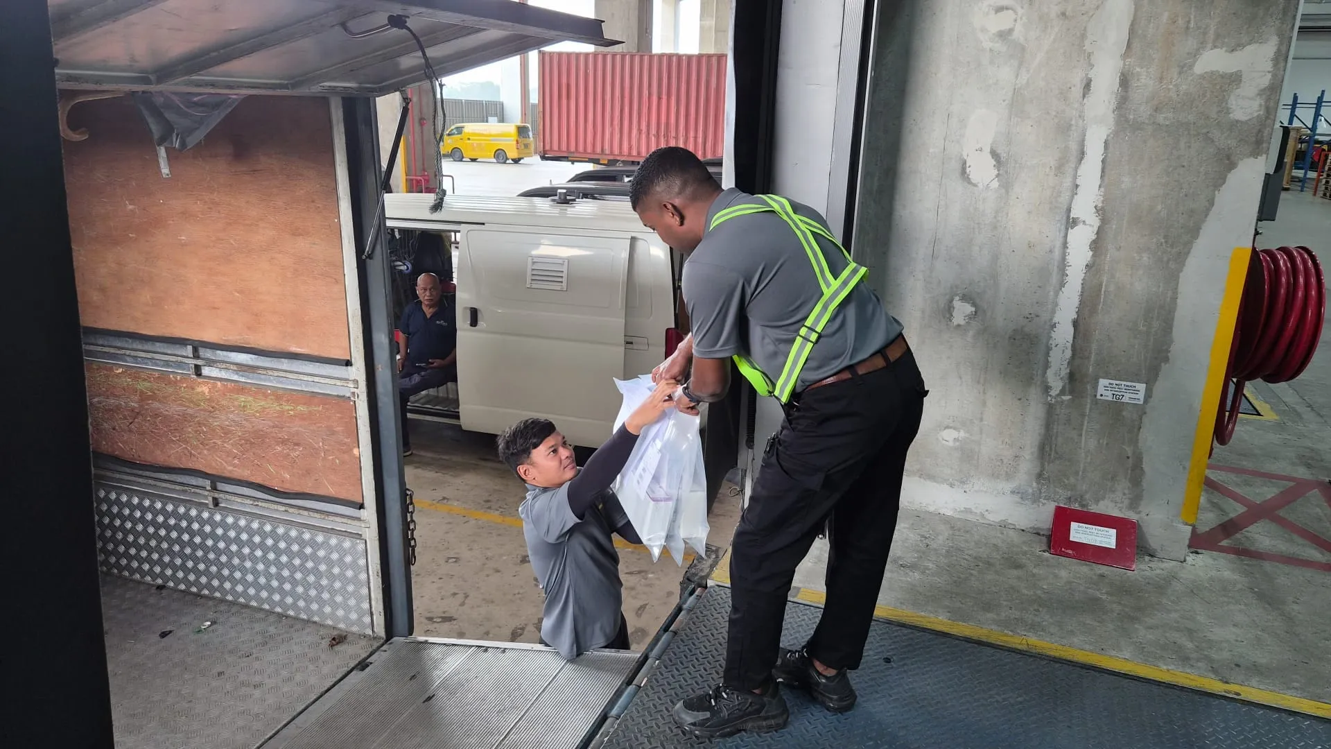 SRM Logistics driver in a hi-vis harness handing a sealed parcel down from a lorry tailgate to a colleague at a loading dock