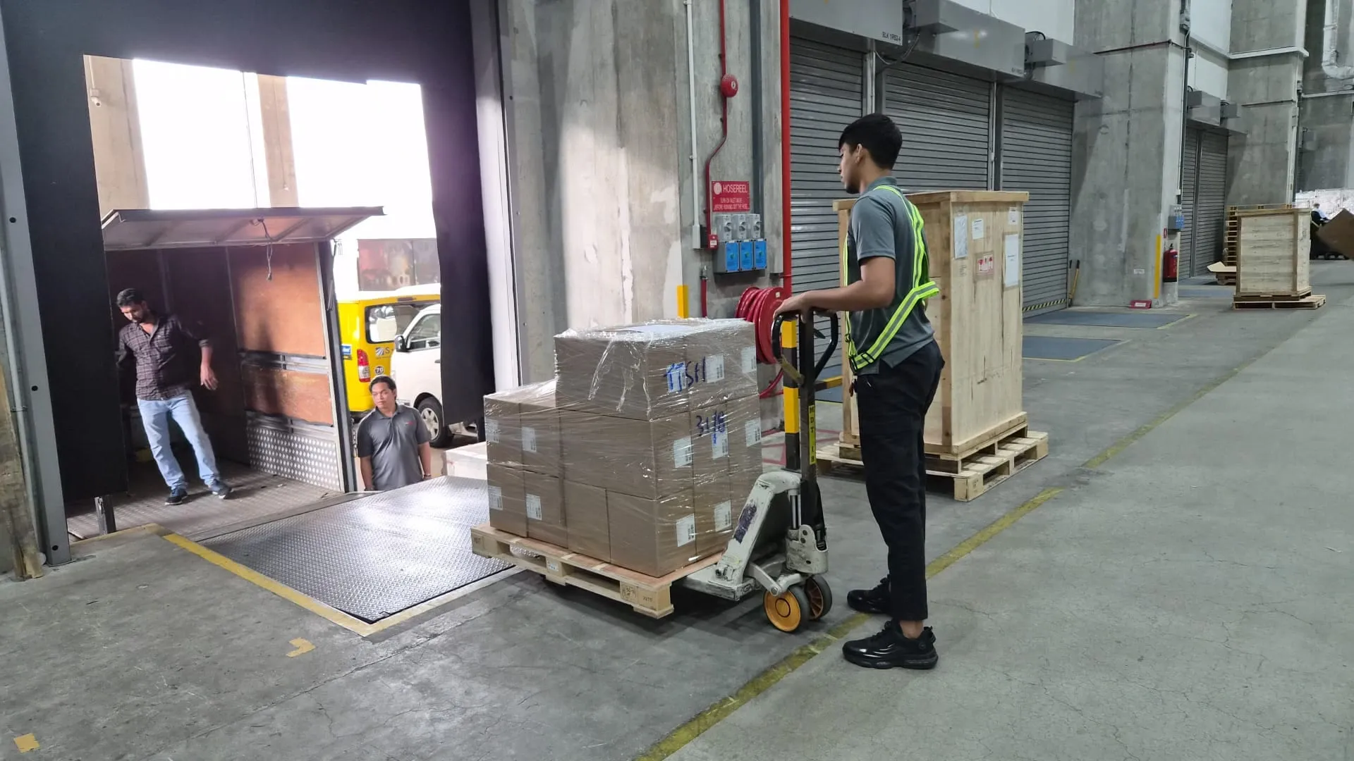 SRM Logistics driver steering a pallet jack loaded with a shrink-wrapped pallet of cartons across a warehouse loading dock