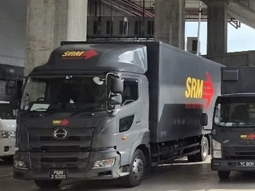 The 24-ft Hino box lorry parked in the yard, the yellow SRM wordmark and red arrow printed large along the side of its box body