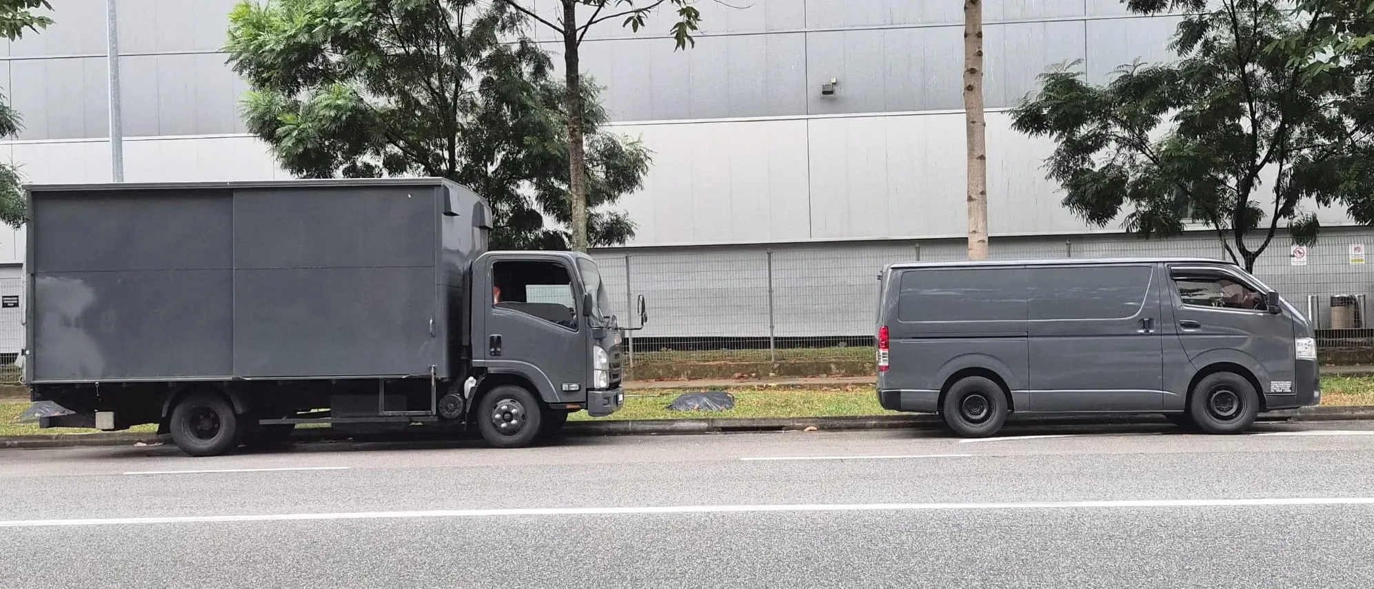 An SRM Logistics Isuzu box lorry and a Toyota Hiace van parked nose to tail at a Singapore kerb, photographed side-on from one position so their lengths compare directly