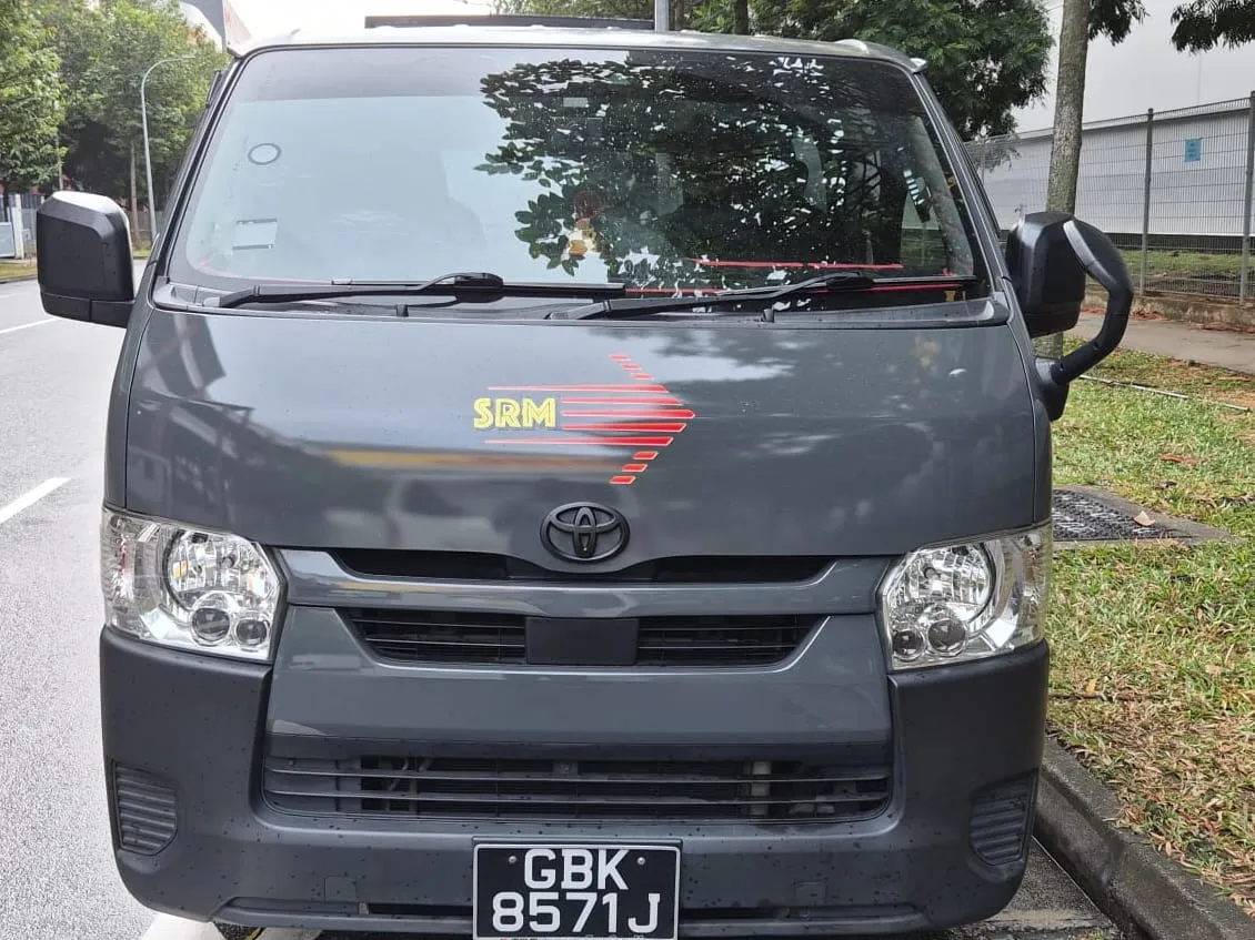 Toyota Hiace van in SRM Logistics livery photographed head-on at the kerb, the yellow SRM wordmark and red speed-line arrow on the bonnet